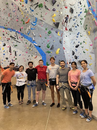 Interns and team members from Tex-Em-All stand in front of a rock climbing wall during an intern event.